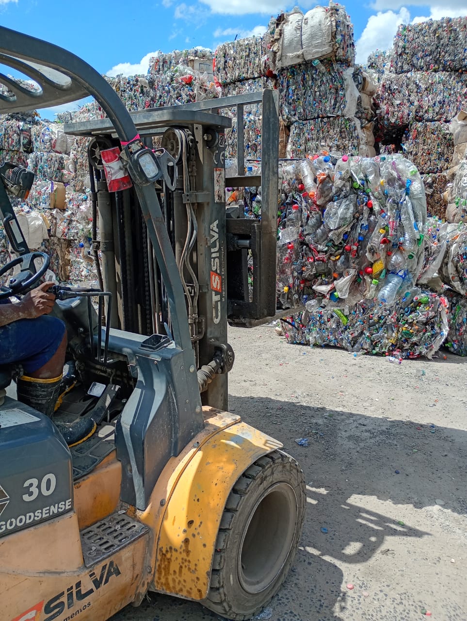 Empilhadeira transportando fardos de materiais recicláveis compactados no pátio da empresa parceira